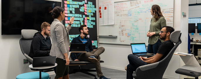 Five diverse technology associates collaborate with sticky notes and a whiteboard.