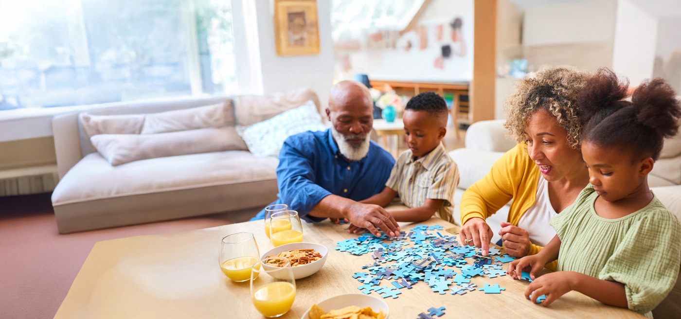 A retirement-aged couple assembling a puzzle with their two grandchildren.