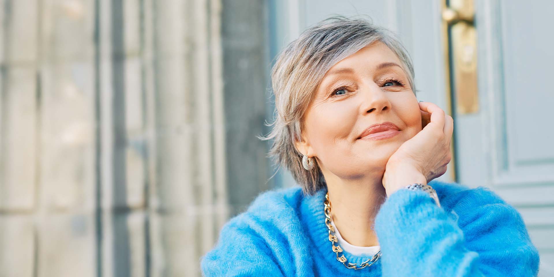 close up of an older woman smiling and resting her chin on her hand at a table