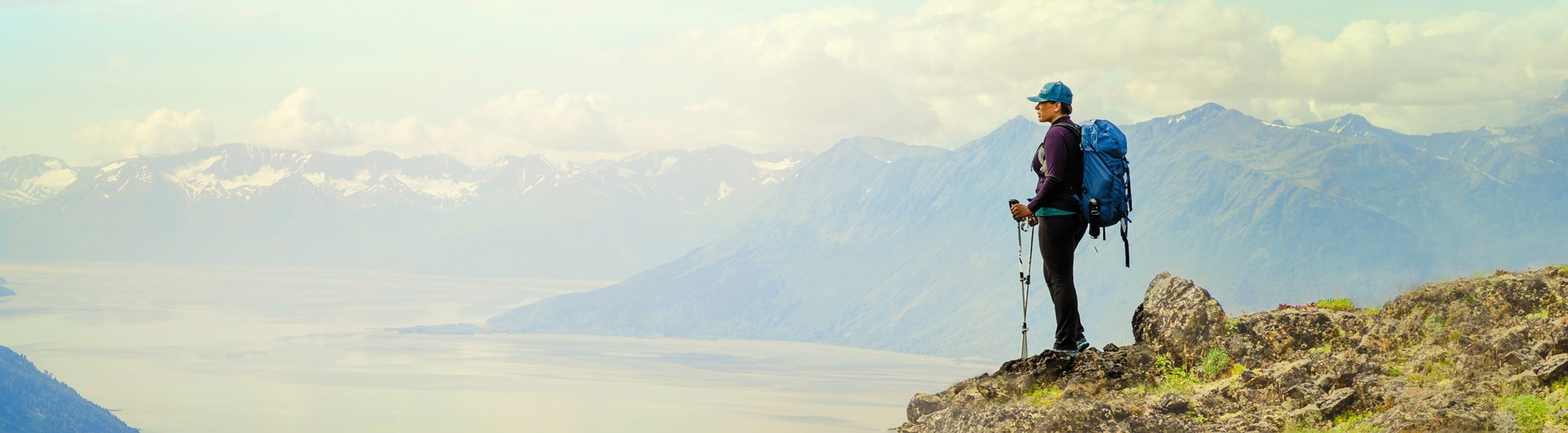 hiker looking out on the top of a moutain with hiking poles and a large backpack