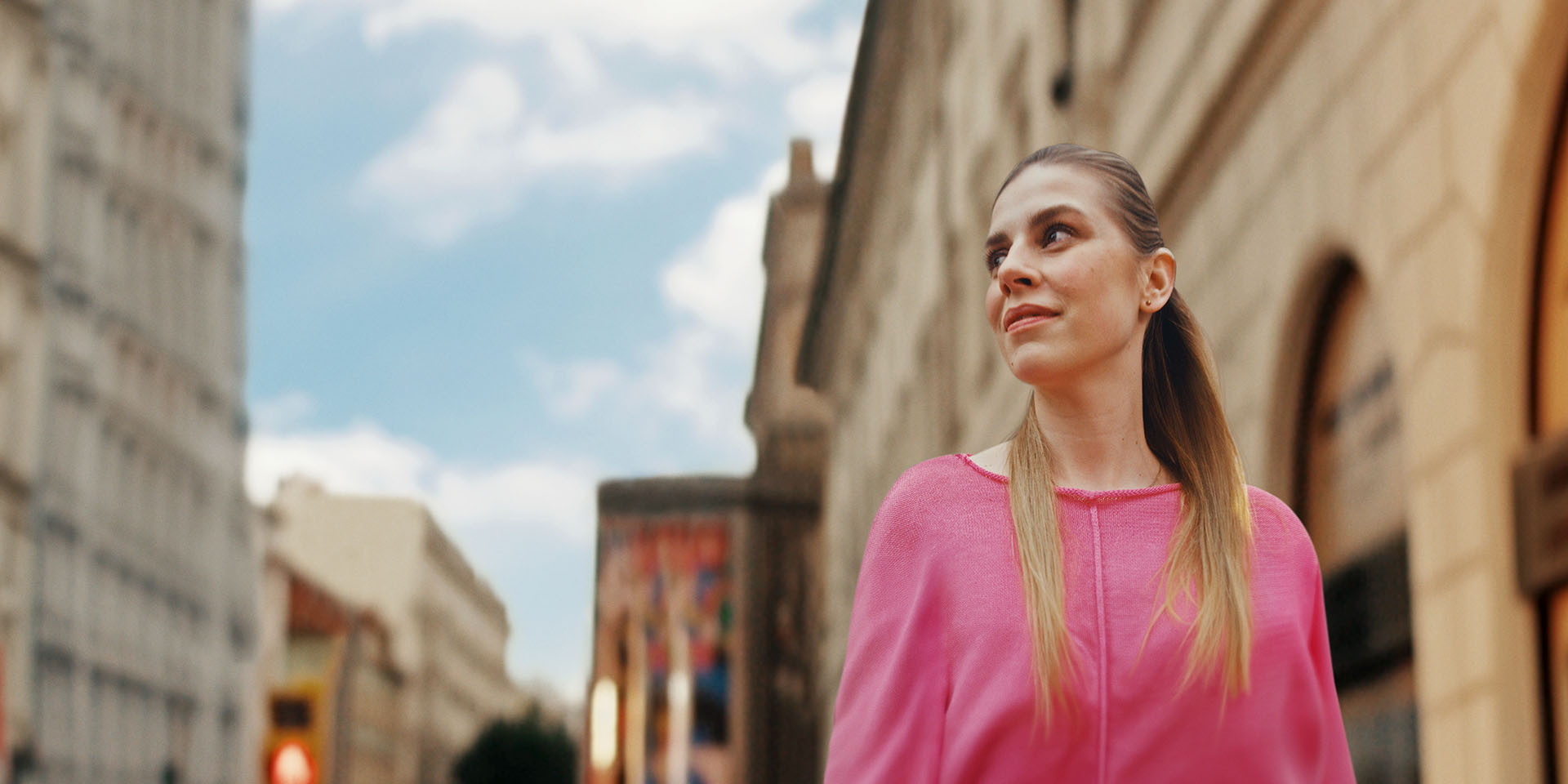 A woman in a city is looking sideways into the distance with a restful expression on her face.