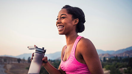 woman smiling and holding water bottle while exercising outside