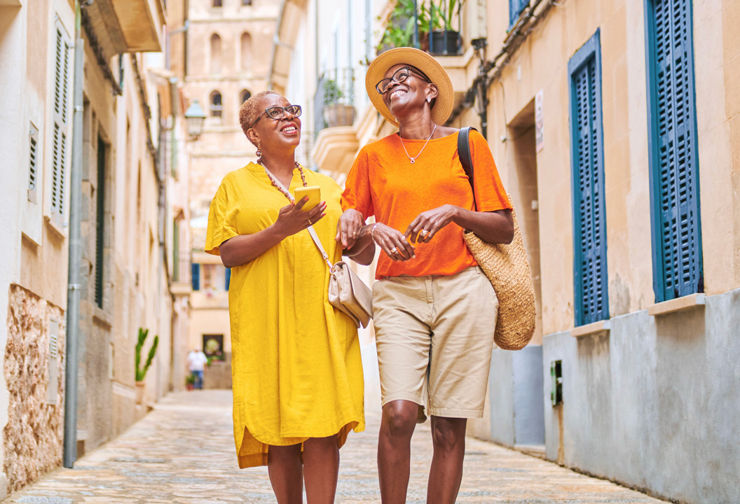 two female friends smiling and walking down a cobblestone street together.