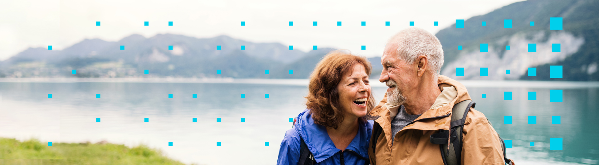 older couple side-hugging and laughing in cold weather hiking gear in front of a scenic mountain lake