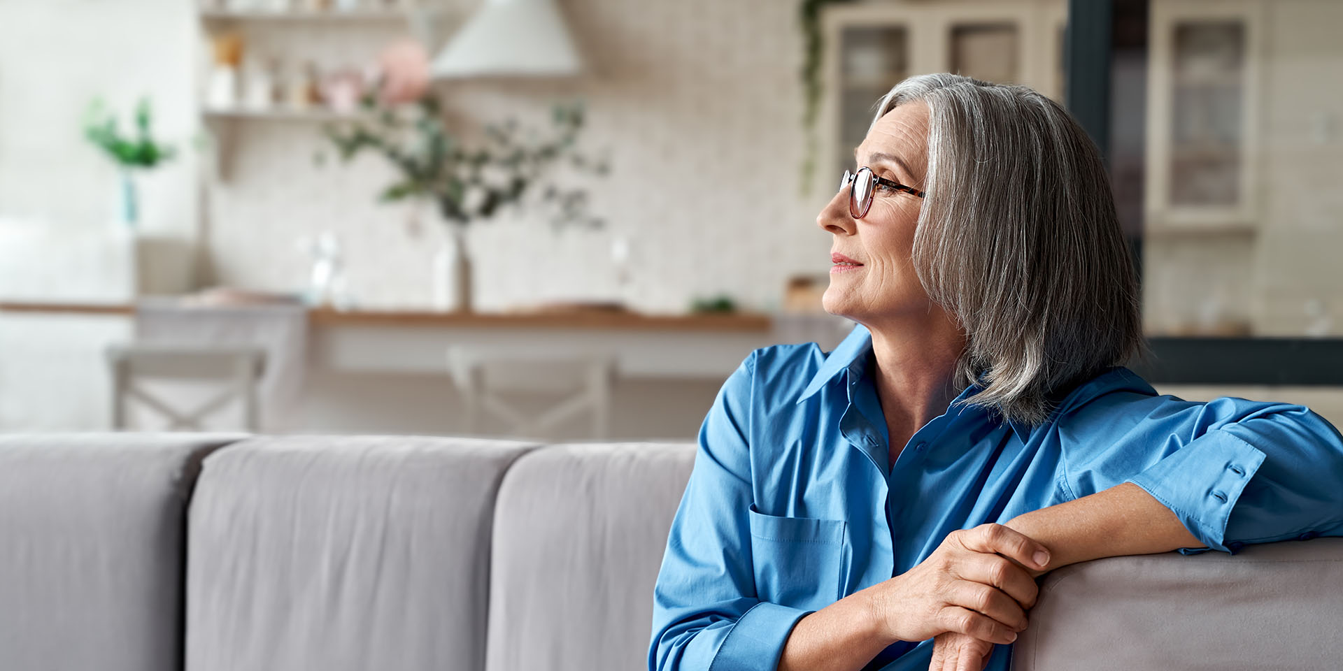 middle-aged woman relaxing with her arm on a couch looking towards a window