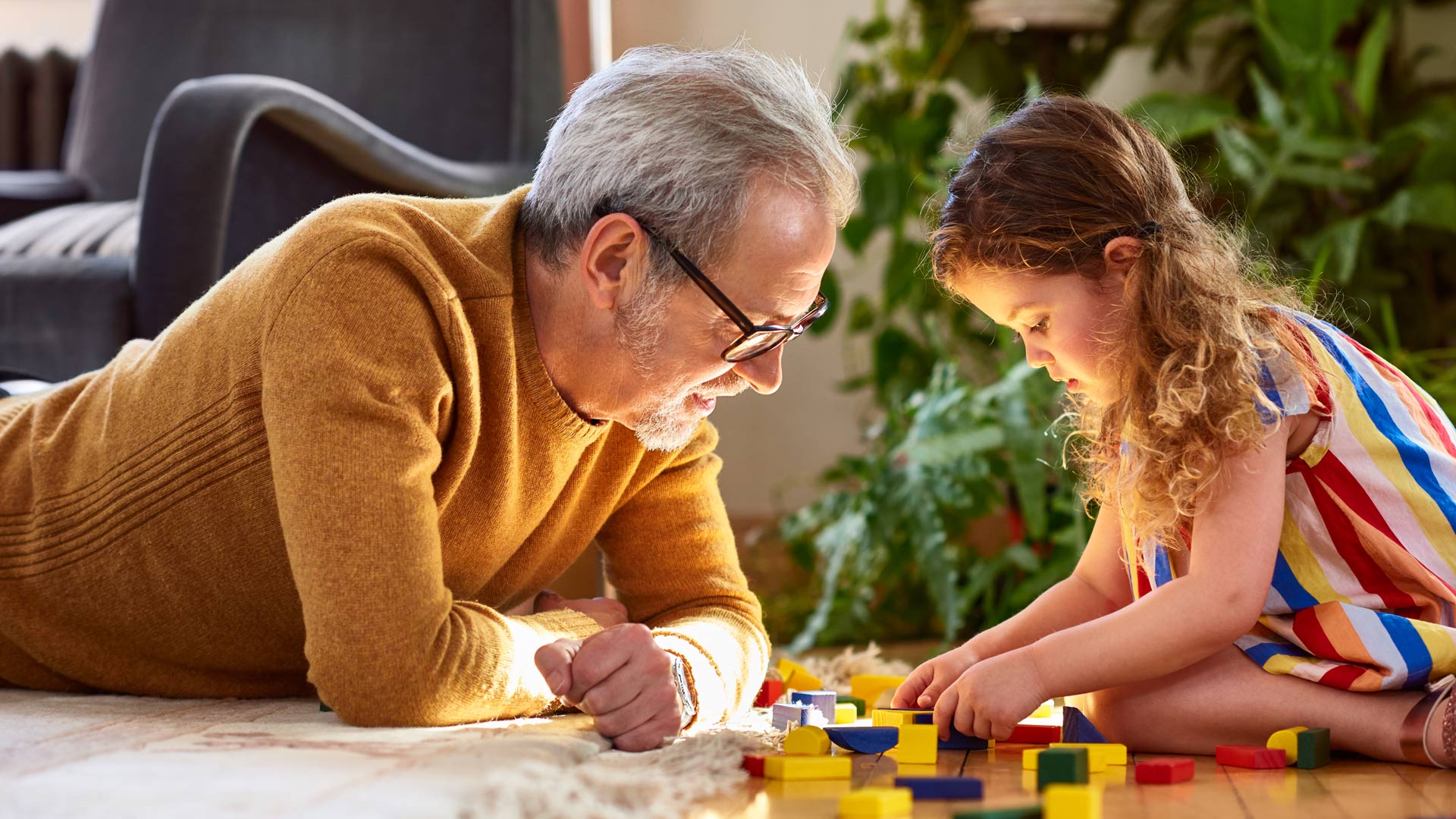 A man lays on the floor across from a little girl as they play a board game together.