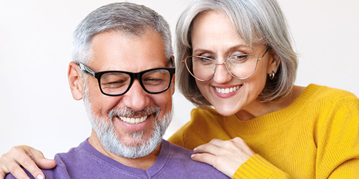 Middle aged woman holding her husbands shoulders, both smiling down at something 