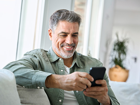 middle age man on his couch smiling while typing on his phone