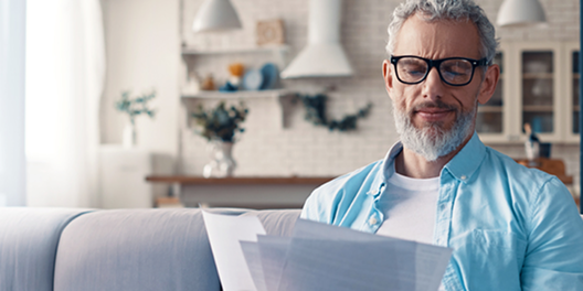 older man with glasses on the couch looking through documents