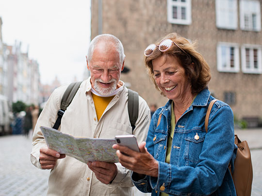 older couple in a city square with backpacks smiling and looking down into a map