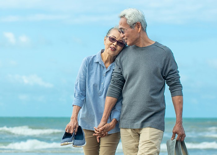 An Asian couple in their 60s walking along the beach
