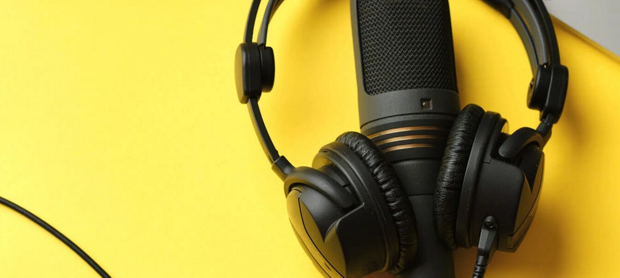 Podcast equipment, including a black microphone and headphones set against a yellow background.