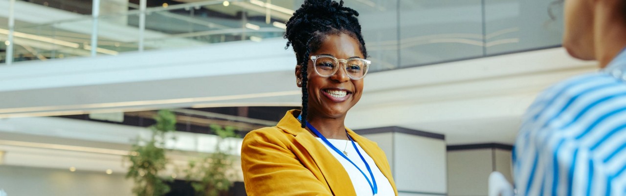 Smiling young professional in a modern office shaking hands with another individual, representing confidence in financial literacy.