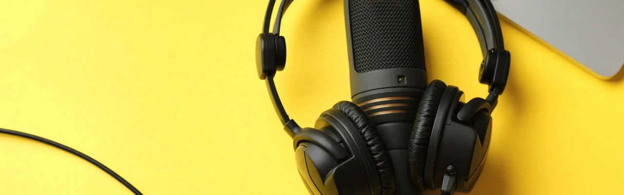 Podcast equipment, including a black microphone and headphones set against a yellow background.